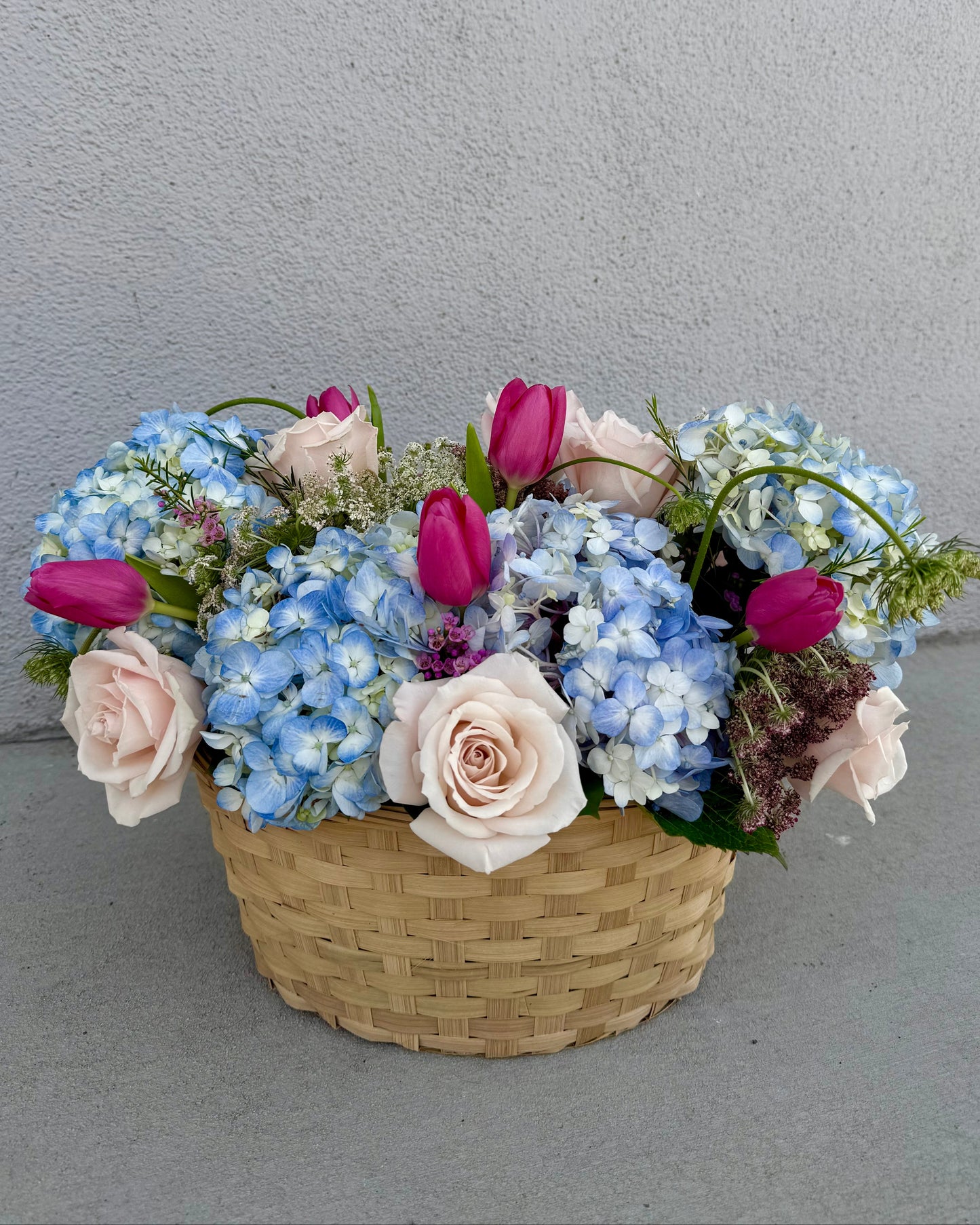 Basket of flowers with hydrangea, roses, tulips, wax flower, and greenery placed in a basket.