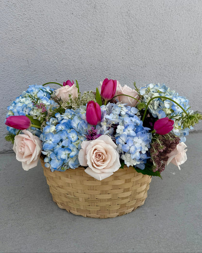 Basket of flowers with hydrangea, roses, tulips, wax flower, and greenery placed in a basket.