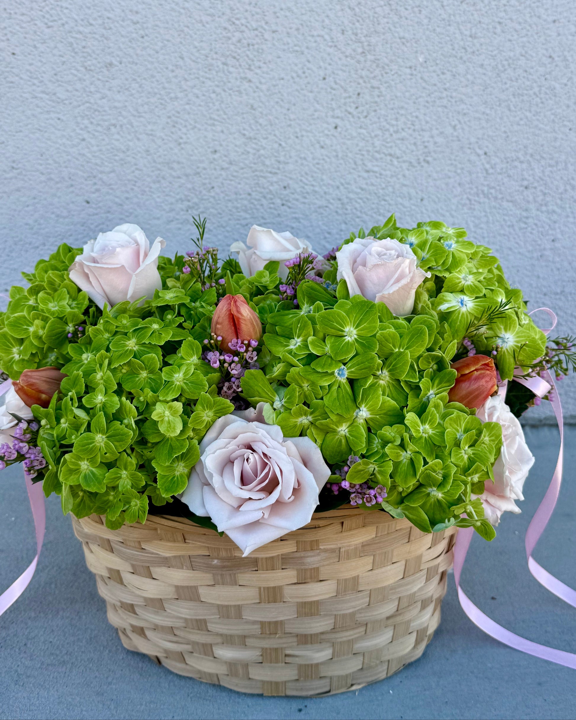 Basket of flowers with hydrangea, roses, tulips, wax flower, and greenery placed in a basket.