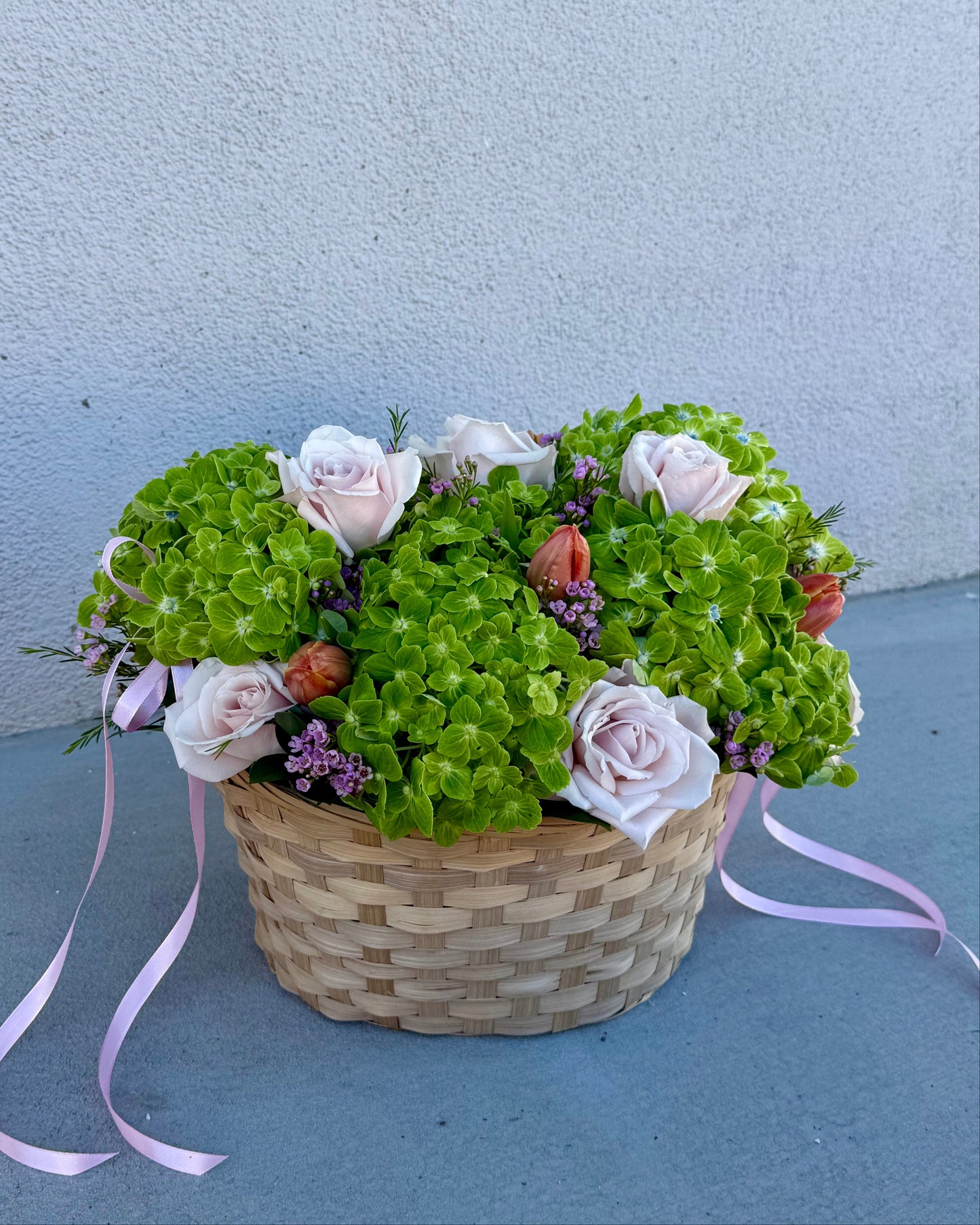 Basket of flowers with hydrangea, roses, tulips, wax flower, and greenery placed in a basket.