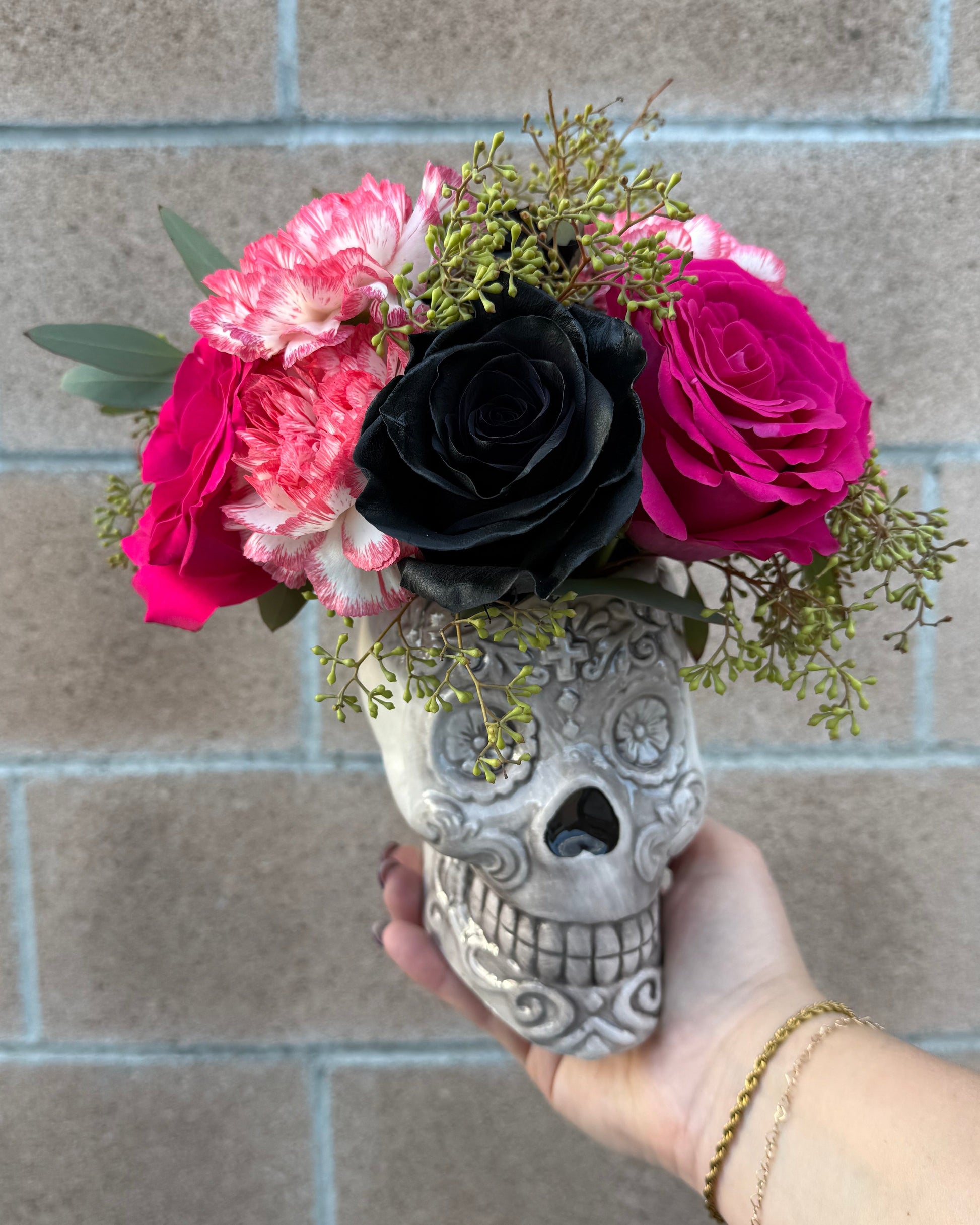 Superbloom Floral skull vase floral arrangement crafted with roses, carnations, mums and similar flowers with various greens, 