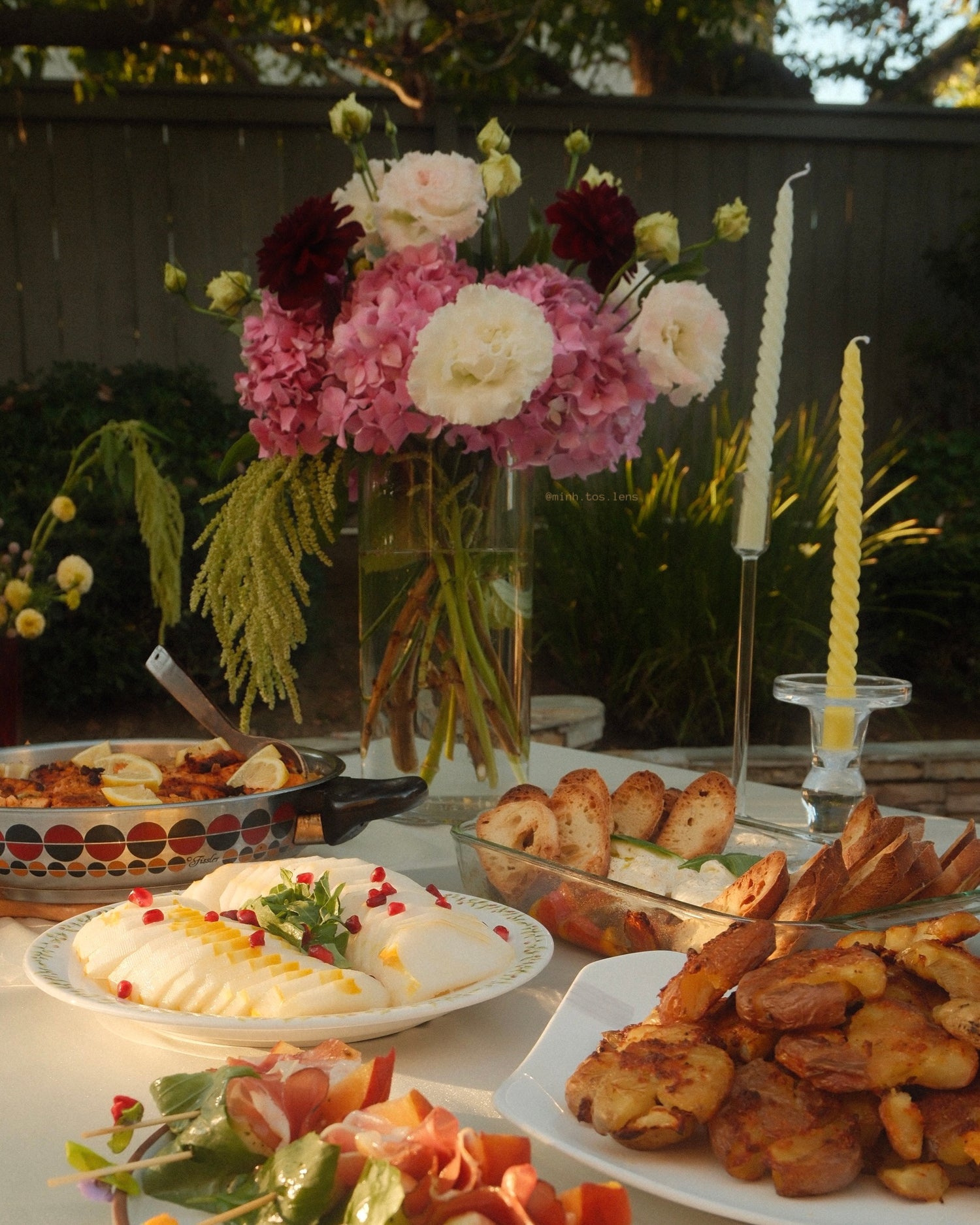 Outdoor setting with a table full of food, including a floral arrangement and candles.