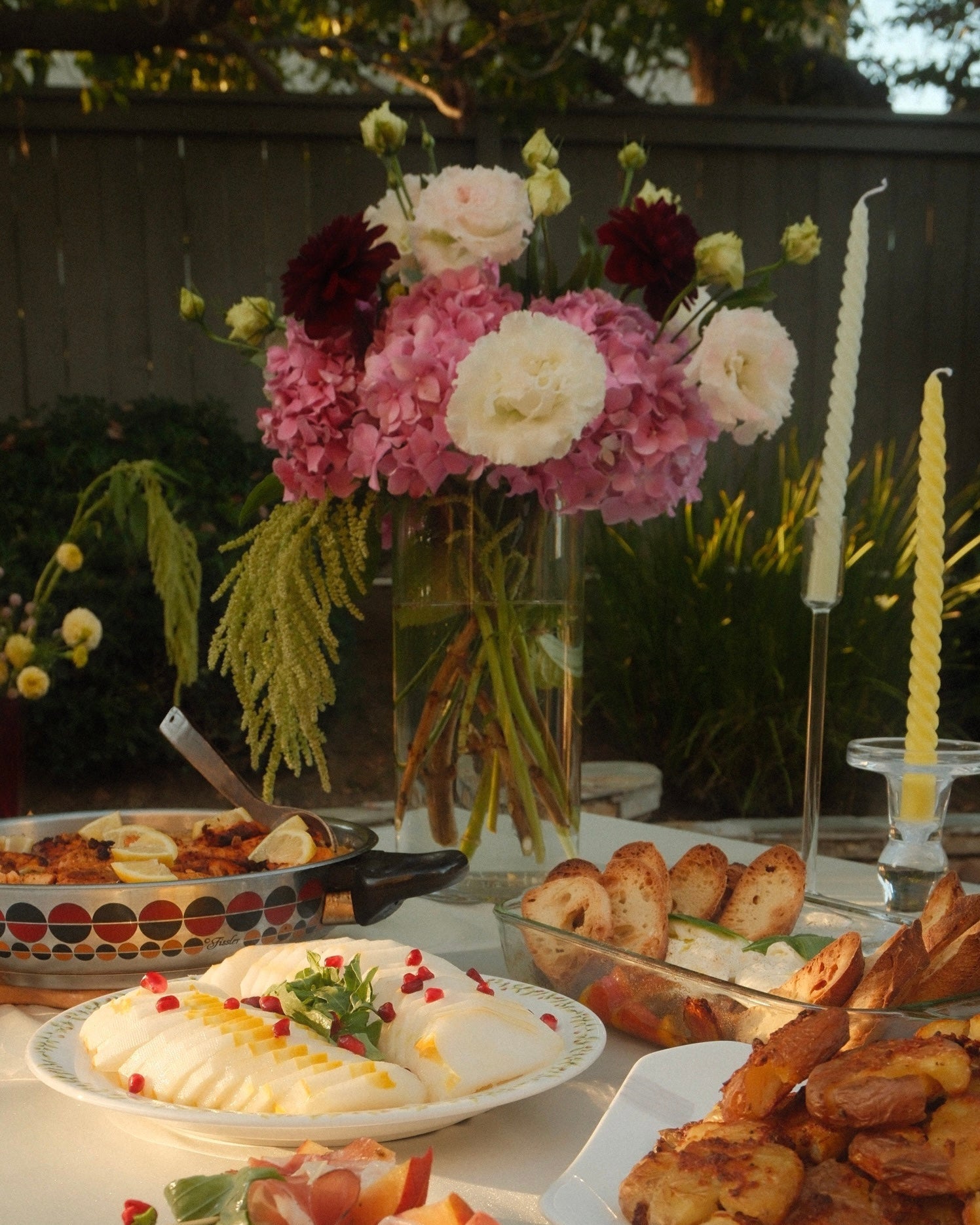 Outdoor table setting with food, flowers, and candles