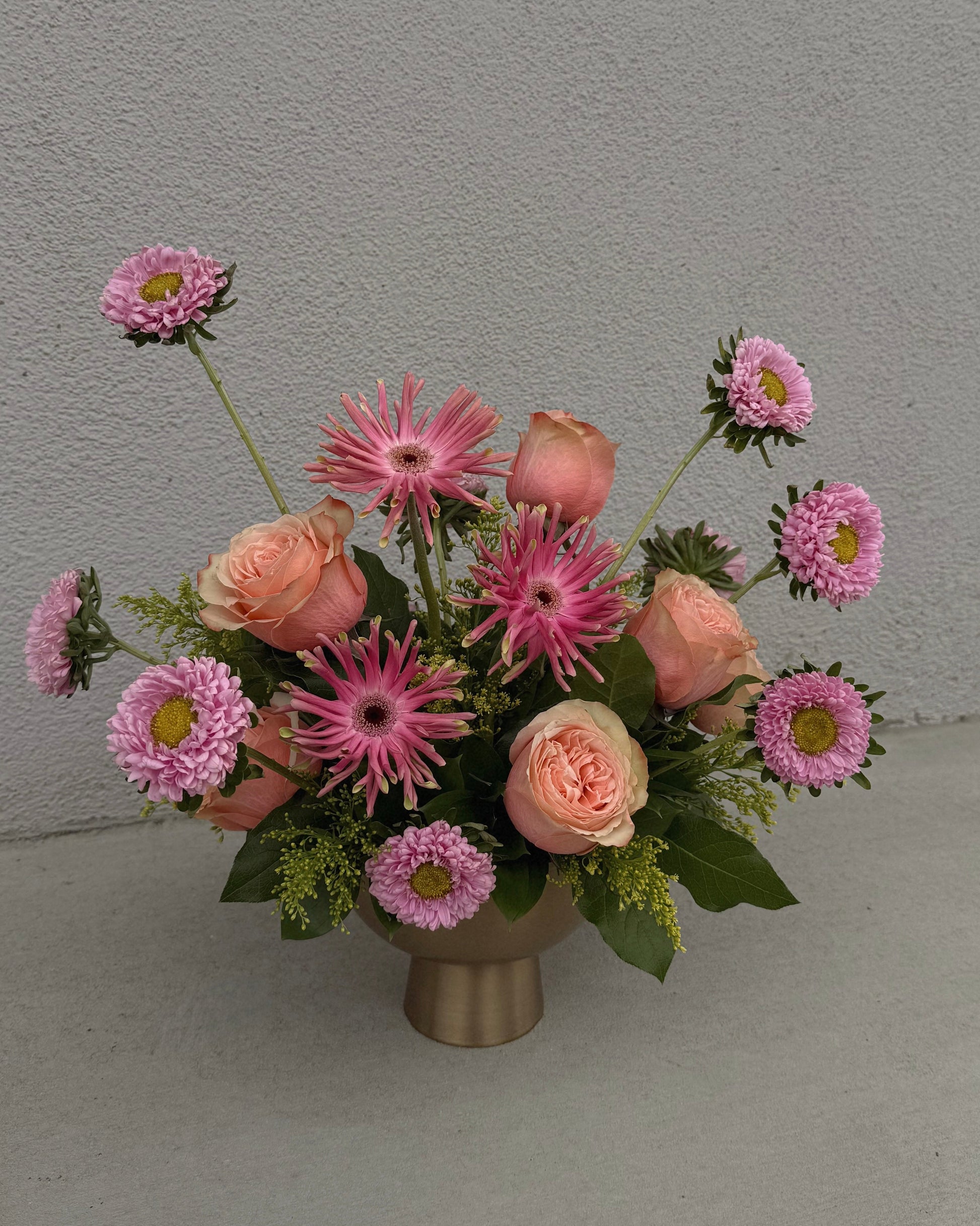 Bouquet of pink and peach flowers in a gold vase.