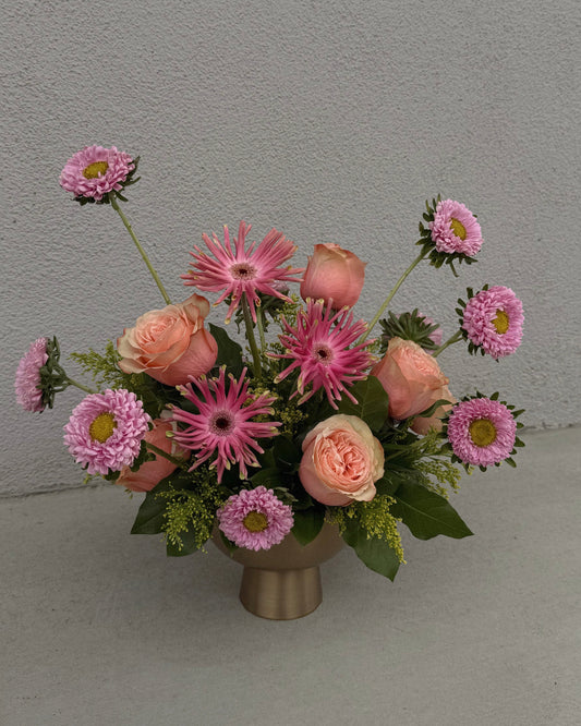 Bouquet of pink and peach flowers in a gold vase.