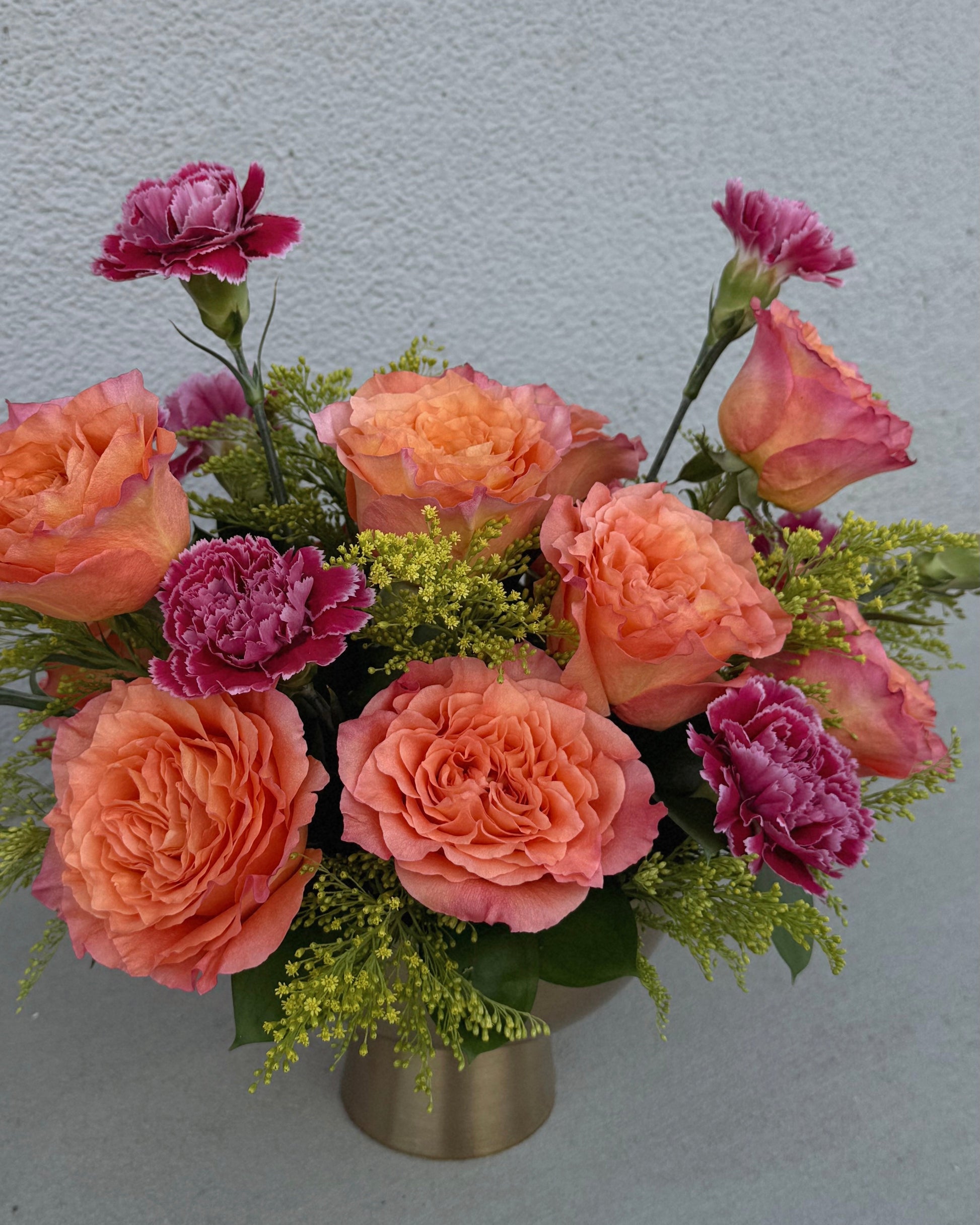 Arrangement of pink carnations and orange garden roses with yellow solidago  in a gold vase