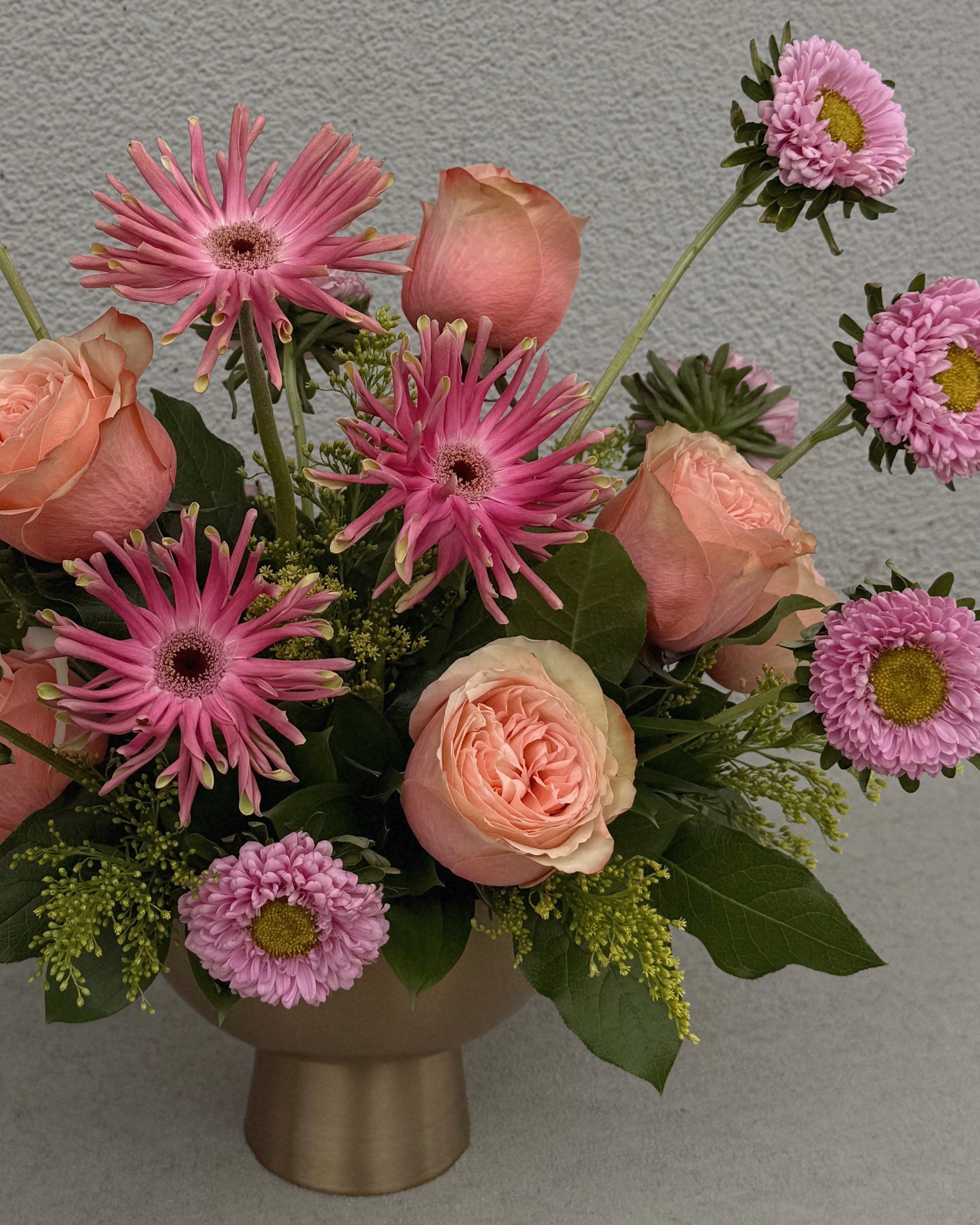 Bouquet of pink and peach flowers in a gold vase.