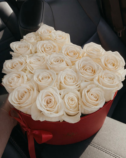 Bouquet of white roses in a red box held by a person inside a vehicle.