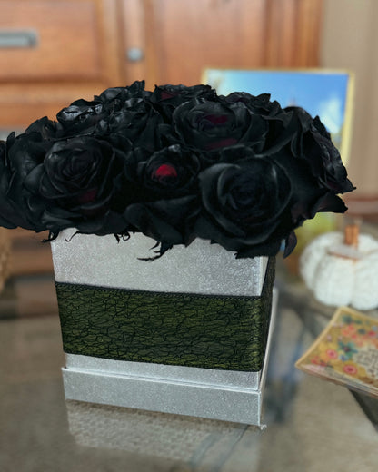 Bouquet of black roses in a decorative box on a reflective surface with a blurred background.
