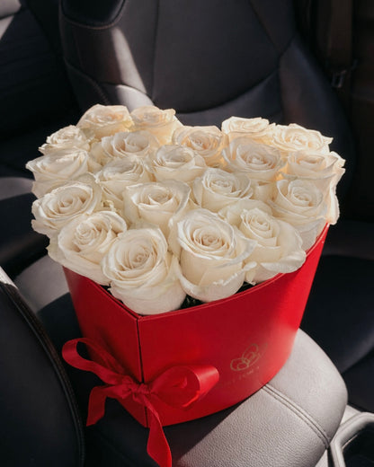 Heart-shaped box of white roses with a red bow on a car seat.