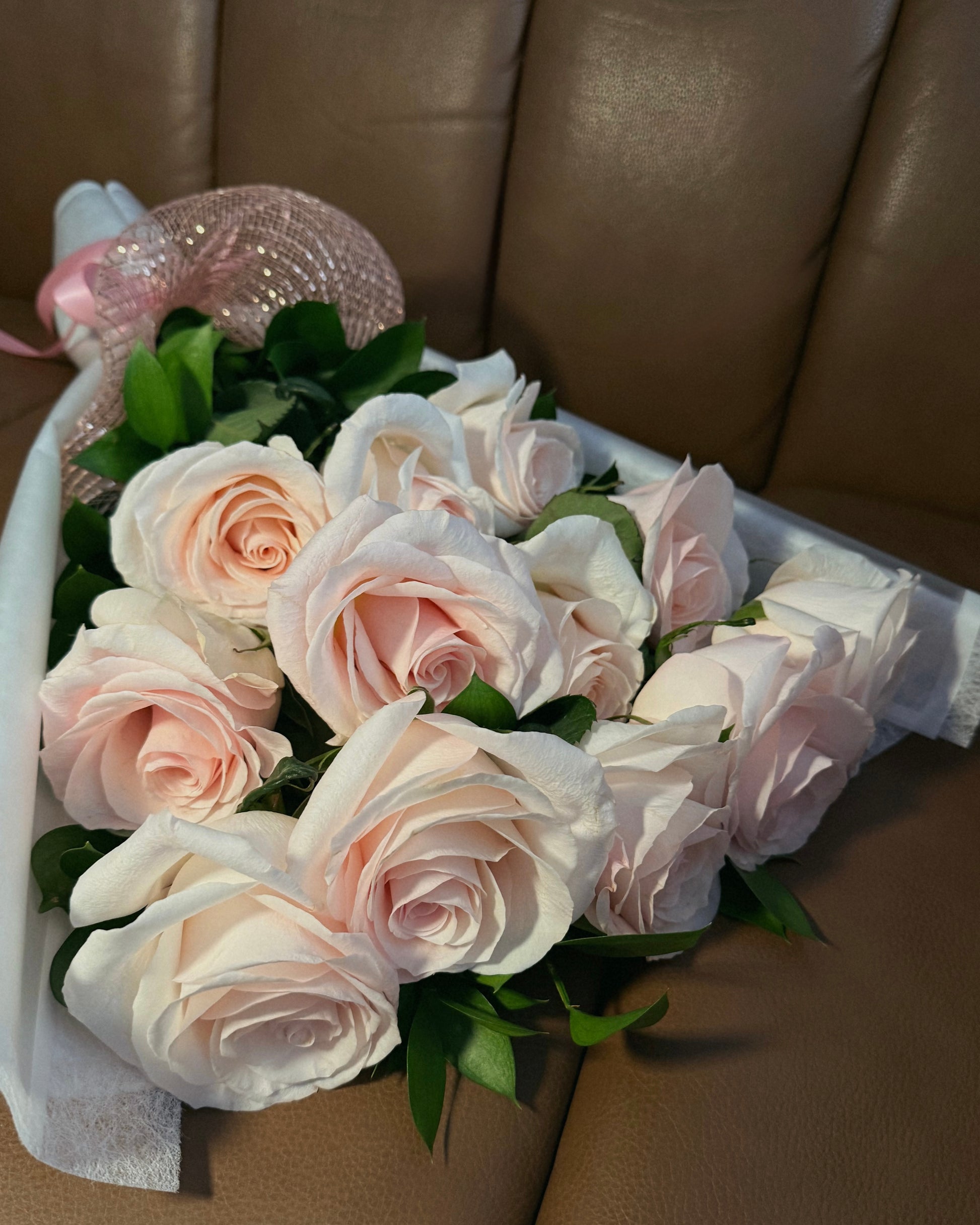 Bouquet of pink roses with greenery against a brown leather background.