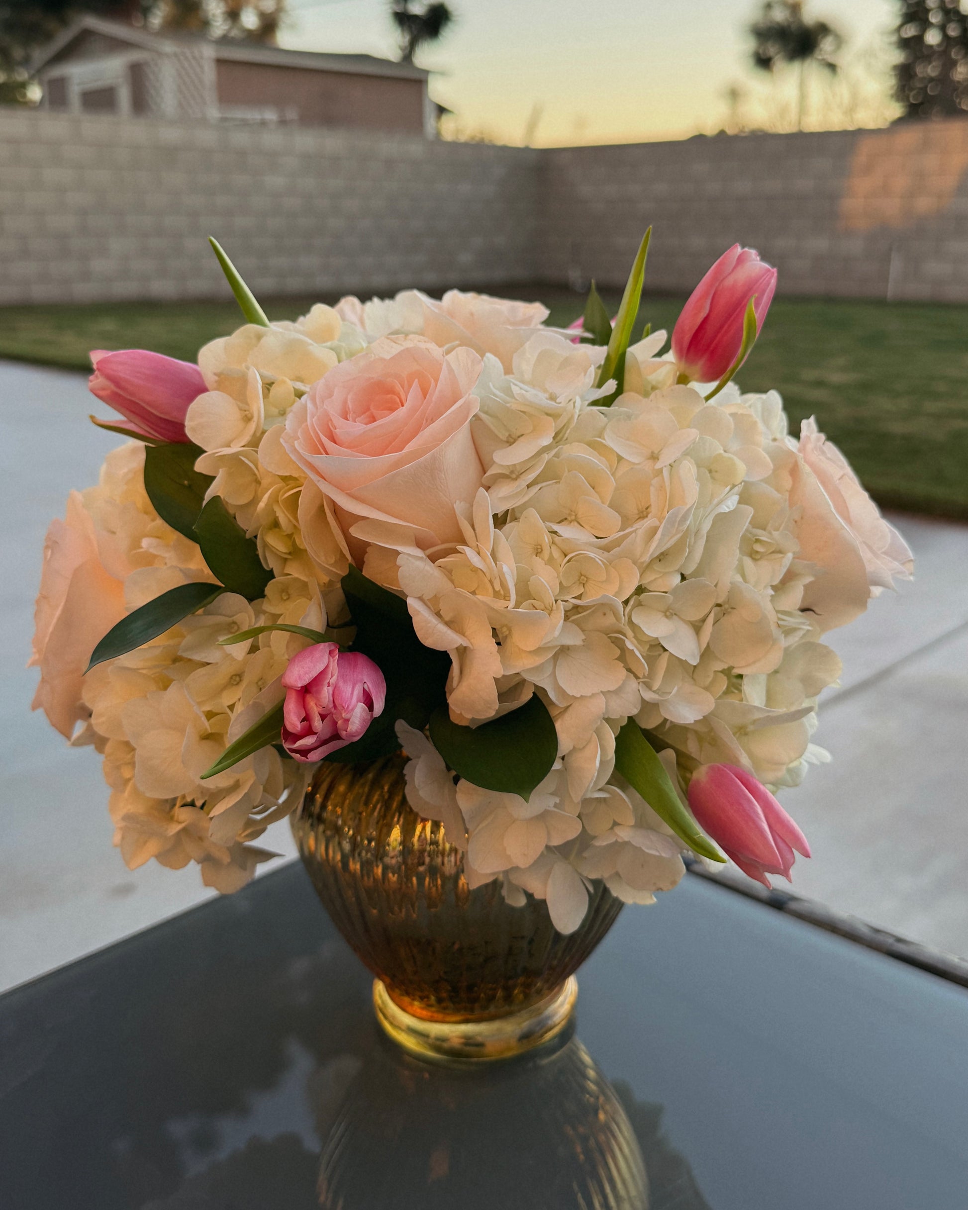 Bouquet of flowers in a vase on a reflective surface with a blurred outdoor background
