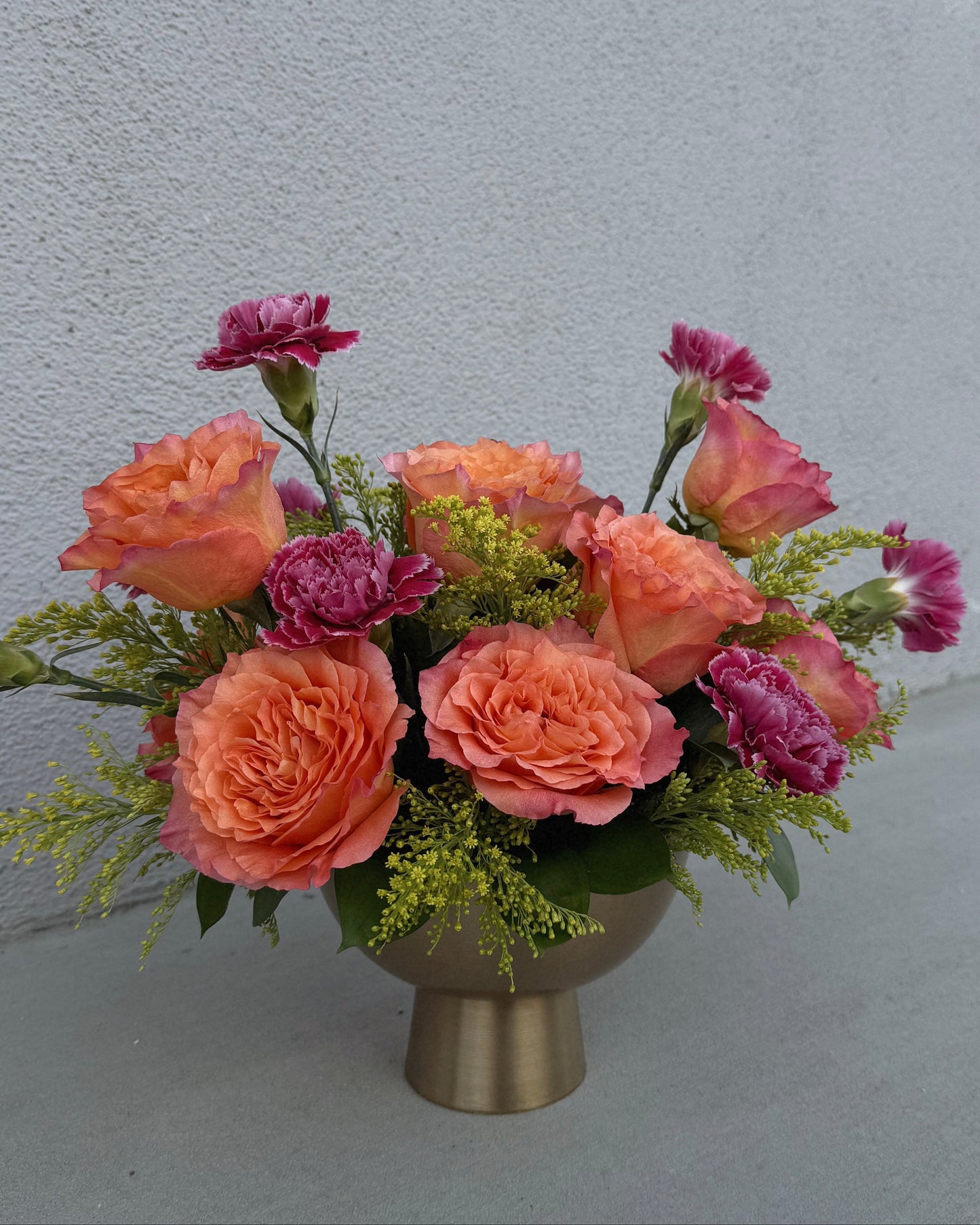 Arrangement of pink carnations and orange garden roses with yellow solidago  in a gold vase