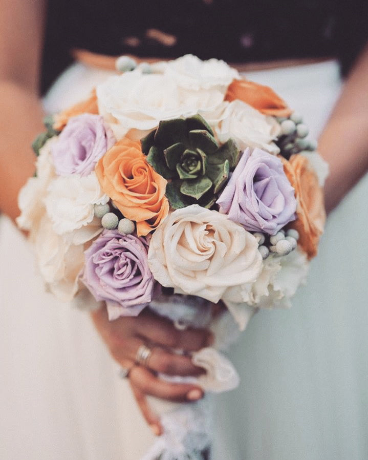 Bouquet of flowers with roses and succulents held by a person.