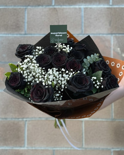 Bouquet of dark roses with baby's breath and greenery against a brick background.